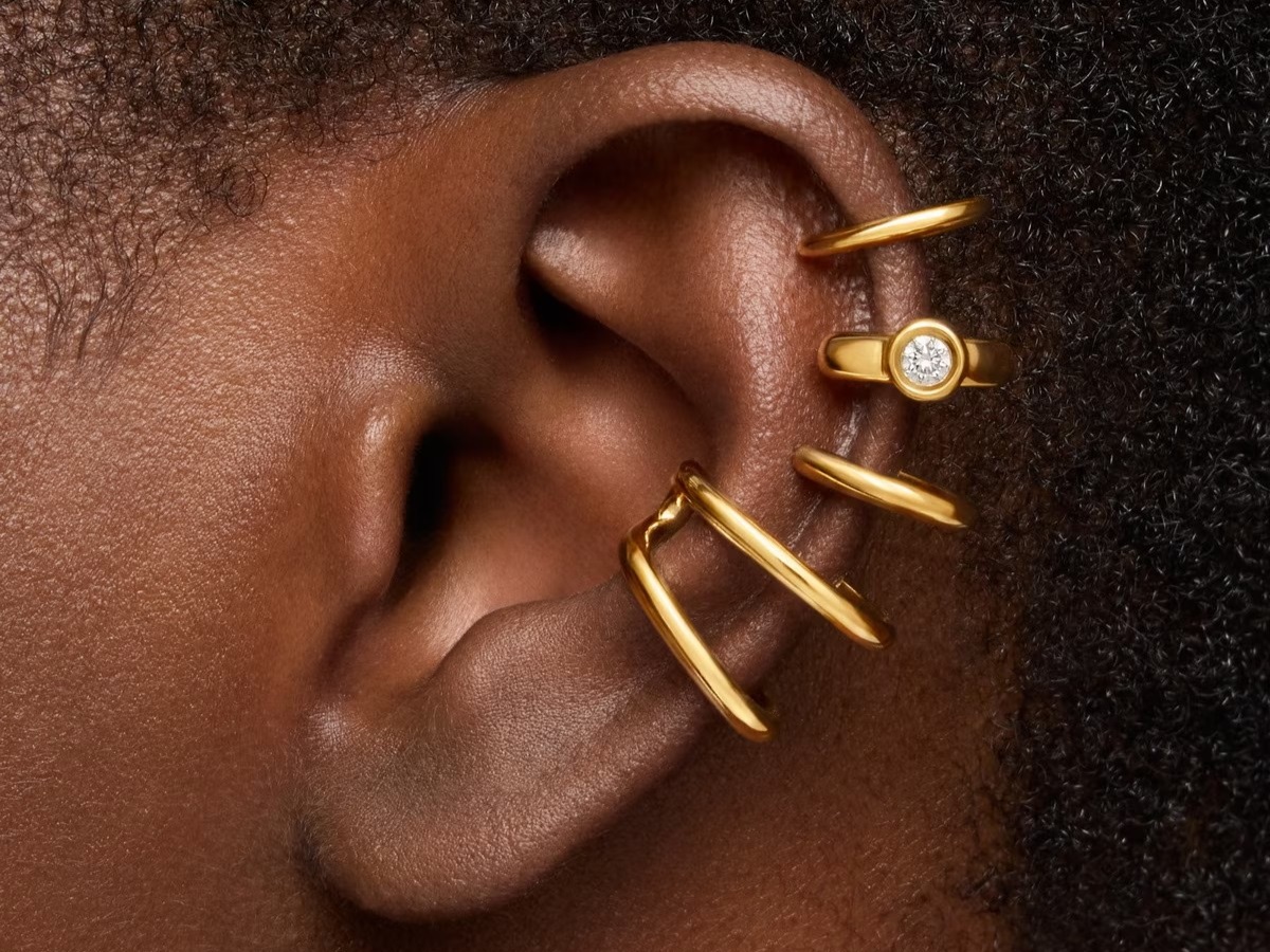 Kobiece ucho ozdobione pozłacanymi kolczykami TOUS ze srebra vermeil