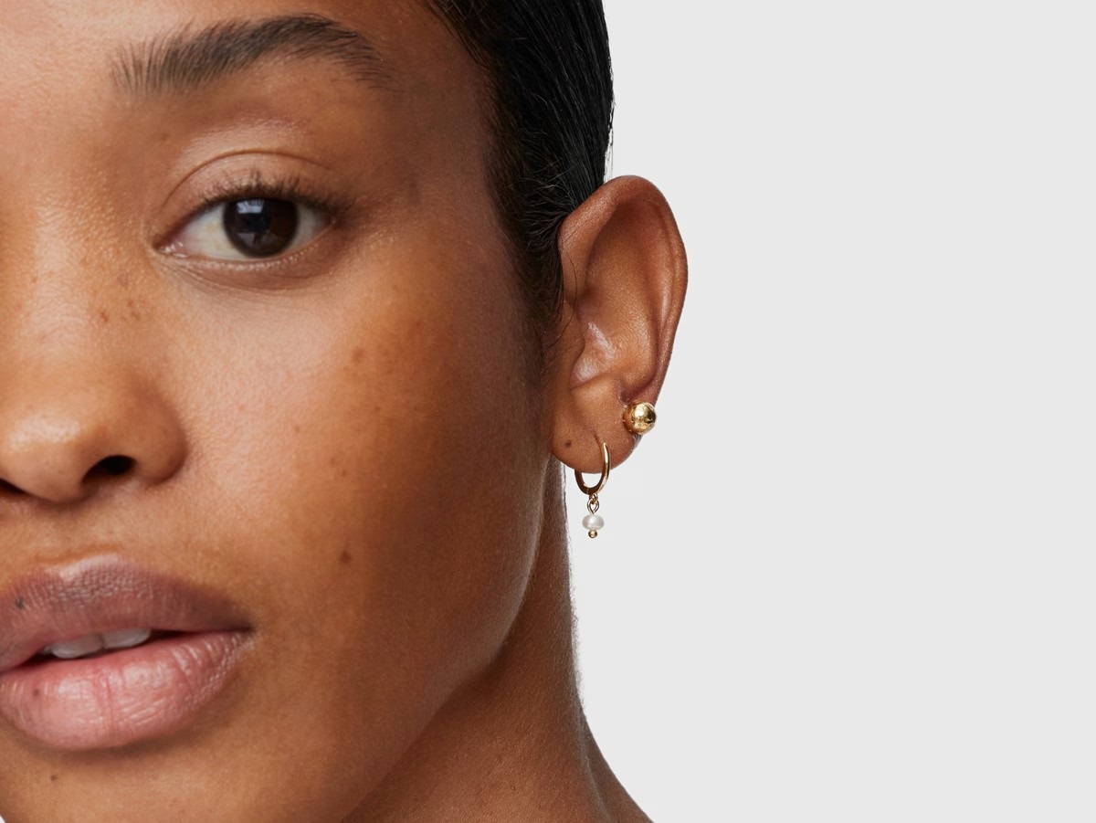 Kobieta ze złotymi kolczykami na uchu - złote kolczyki kółka z perłą i złote kolczyki sztyfty