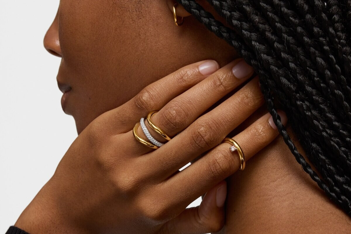 Kobieta dotyka szyi, prezentując kilka złotych obrączek z kamieniami na palcach dłoni.