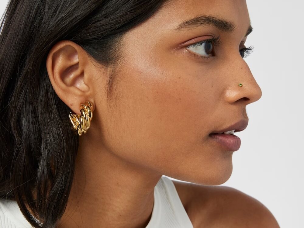 Kobieta obrócona bokiem na białym tle, z kolczykiem do nosa TOUS w nosie
