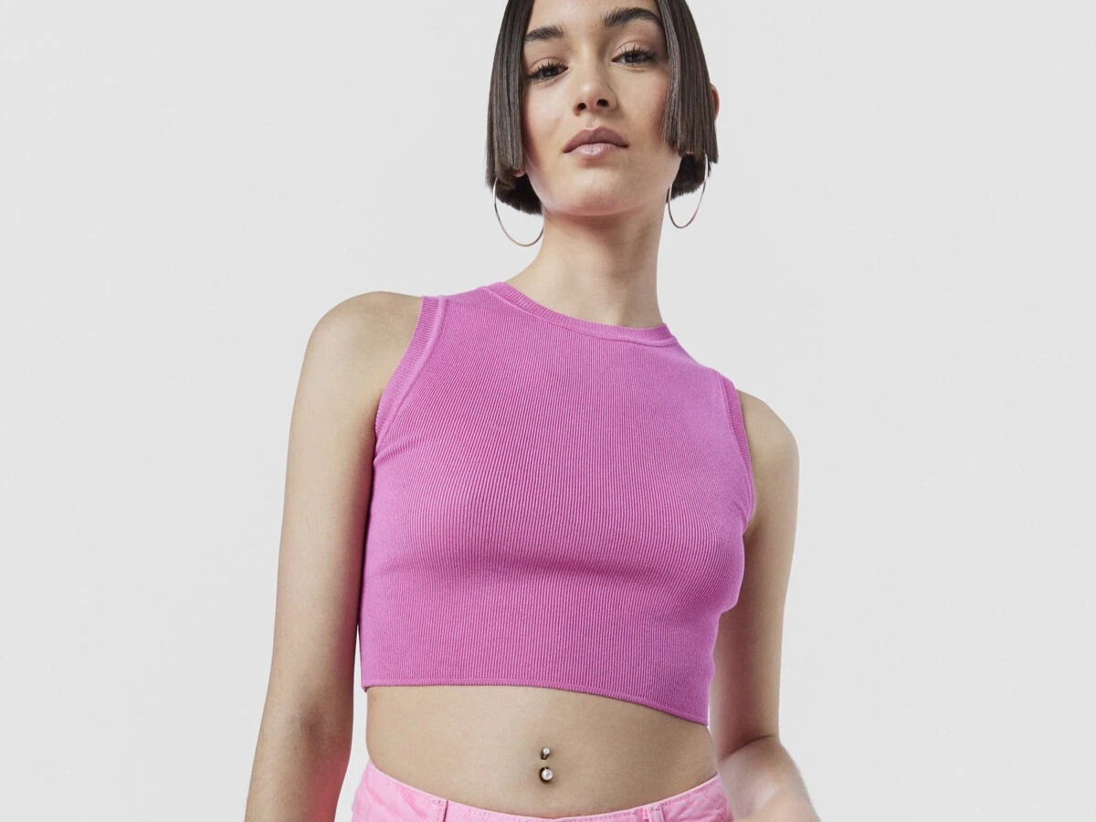 Kobieta w różowym topie na białym tle, z kolczykiem TOUS w pępku