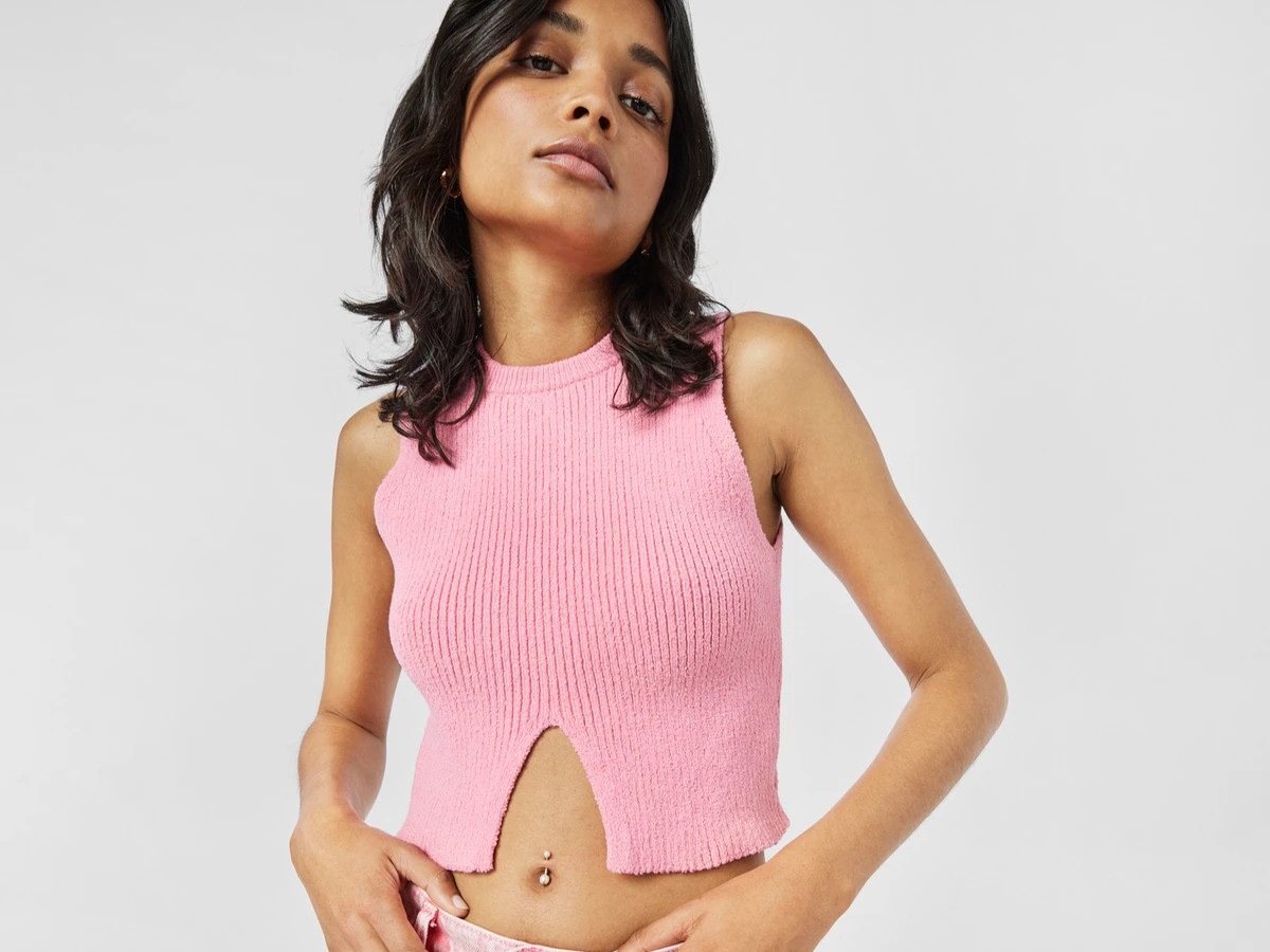 Kobieta w różowej bluzce z kolczykiem TOUS w pępku, na białym tle