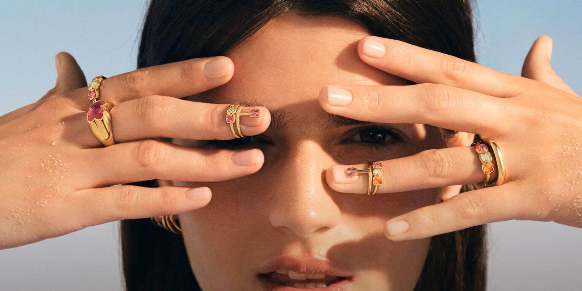 Twarz kobiety przysłonięta dłońmi, które są pokryte złotymi pierścionkami TOUS