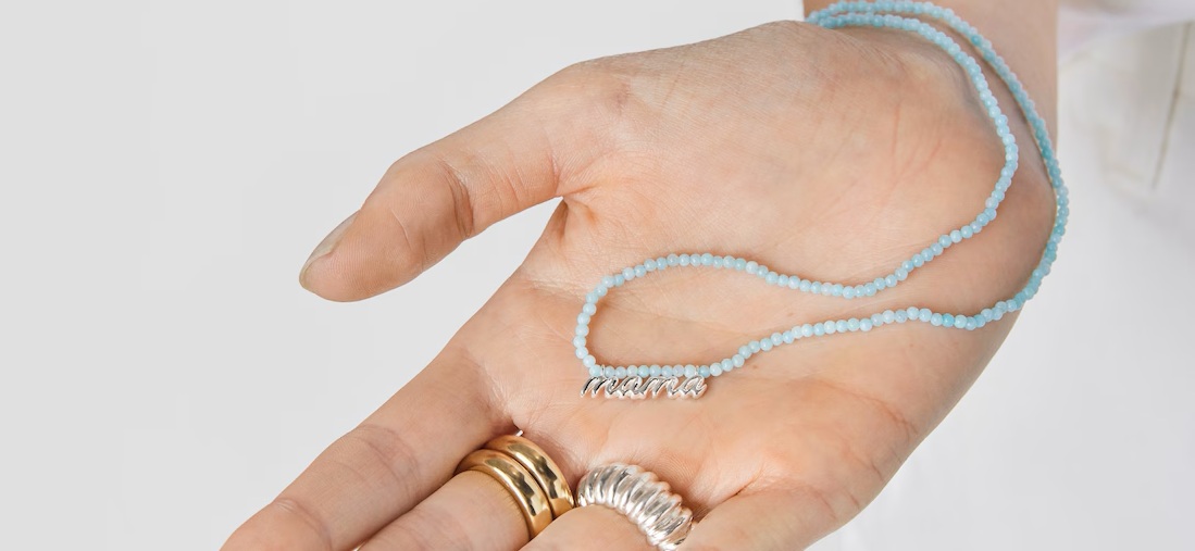 Wyciągnięta dłoń, a na niej naszyjnik TOUS z koralikami z amazonitu i z zawieszką z napisem mama